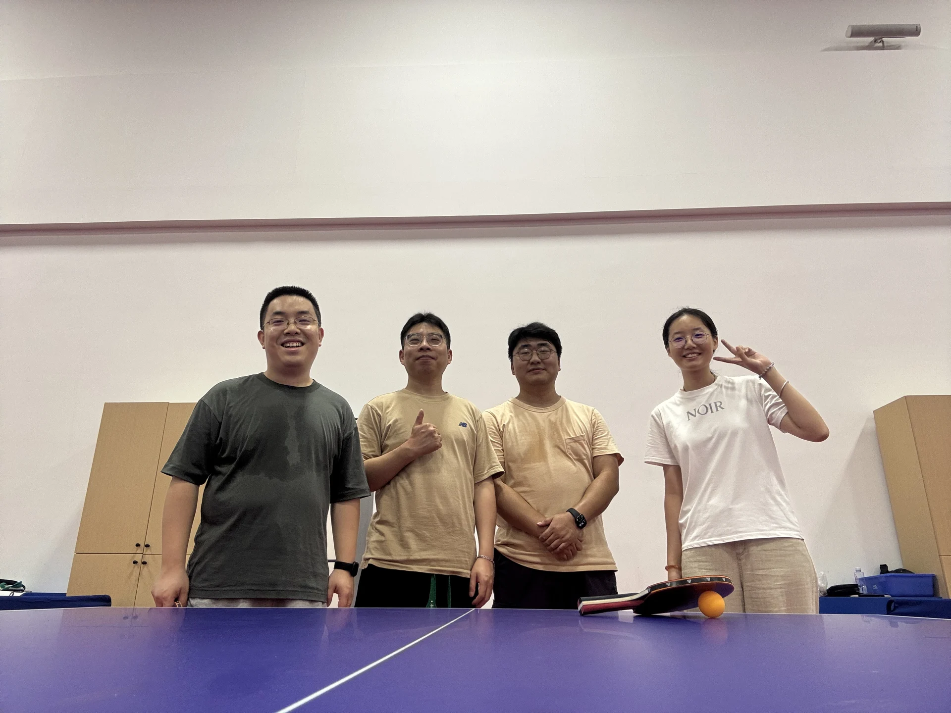 Four group members smiling behind a table tennis table with a paddle and ball.